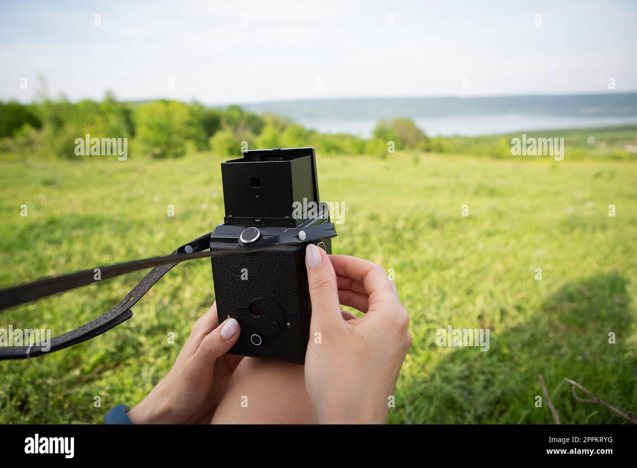 Foto der Hände eines jungen Fotografen mit einer alten Kamera, die eine wunderschöne Landschaft eines Sees und einer grünen Wiese fotografiert. Stockfoto