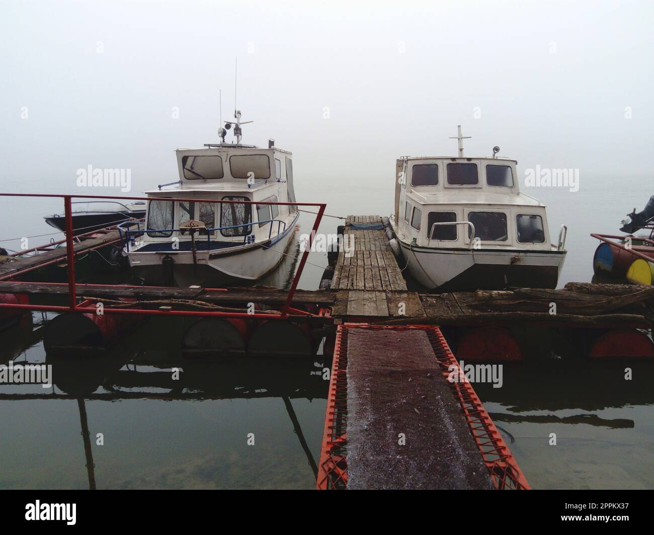 Belgrad, Serbien, 14. Januar 2020 zwei weiße Boote an einem hölzernen Pier, die für den Winter aufbrachen. Nebel-Wetter in Südeuropa. Januar bewölkter Tag. Reflexion des Wassertransports in einem Fluss Stockfoto