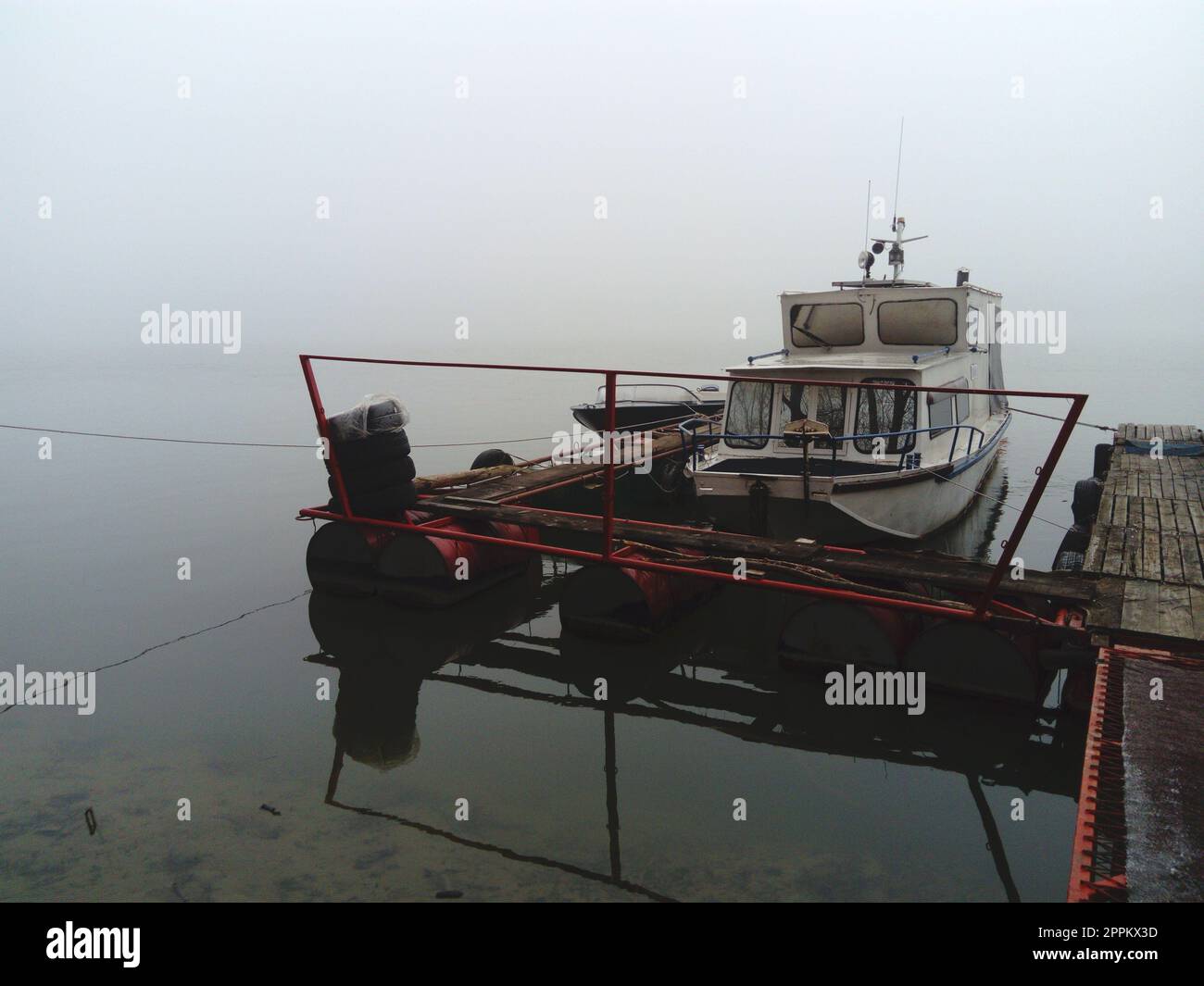 Belgrad, Serbien, 14. Januar 2020 Weißes Boot am Pier, Abfahrt für den Winter. Nebiges Wetter an einem wolkigen Januar-Tag. Reflexion im Fluss. Ein Haus zum Schutz vor dem Wetter Stockfoto