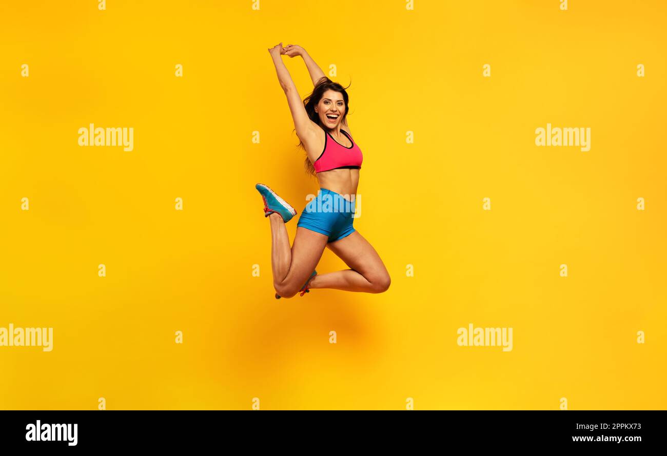 Sportfrau springt auf gelbem Hintergrund. Fröhlicher und fröhlicher Ausdruck. Stockfoto