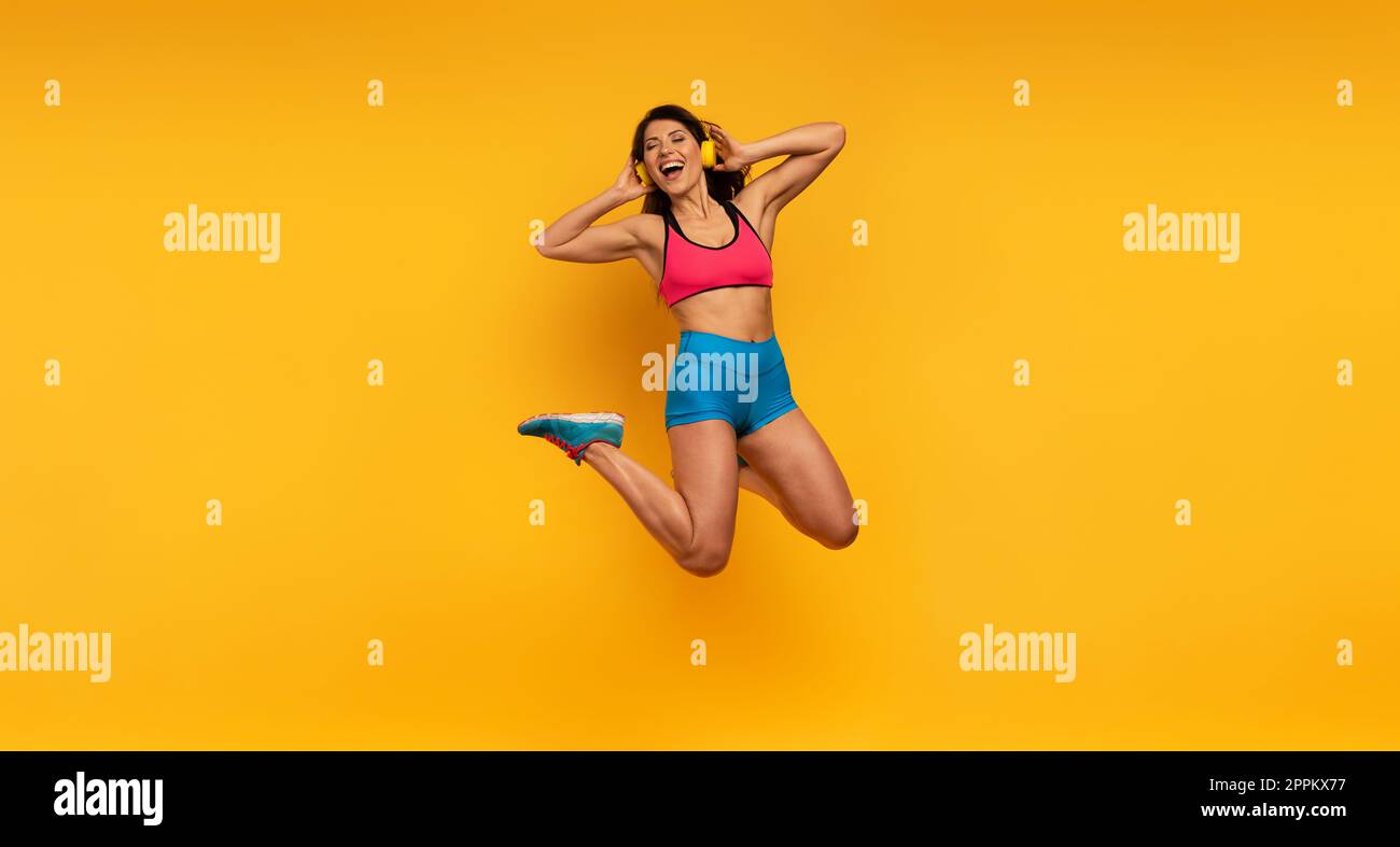 Sport Frau springt auf einem gelben Hintergrund und hören Sie Musik. Fröhlicher und freudiger Ausdruck. Stockfoto