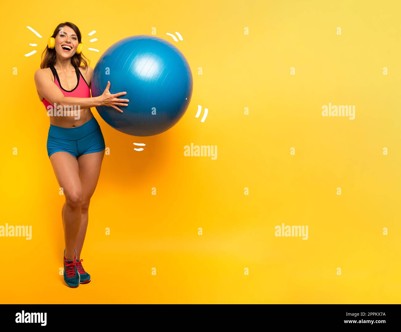 Mädchen mit Headset hält einen Sportball. Gelber Hintergrund Stockfoto