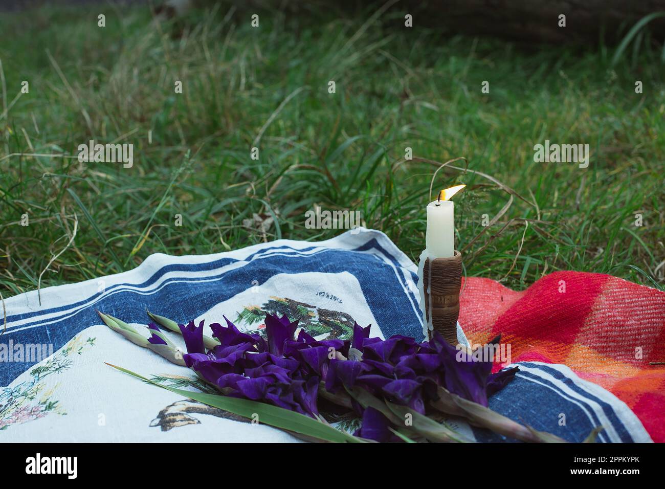 Nahaufnahme der Kerze in einem Holzhalter und verwelkter Gladiolus auf einem Decke Konzeptfoto Stockfoto