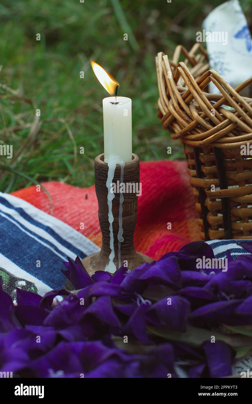 Nahaufnahme brennende Kerze im Holzhalter neben dem Konzeptfoto des gewebten Picknickkorbs Stockfoto