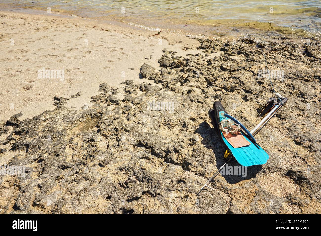 Schnorcheln, Maske, Flossen und einfache Harpune zum Angeln mit Speer am sonnenbeleuchteten felsigen Strand in der Nähe des Meeres, lokale madagassische Fischausrüstung Stockfoto