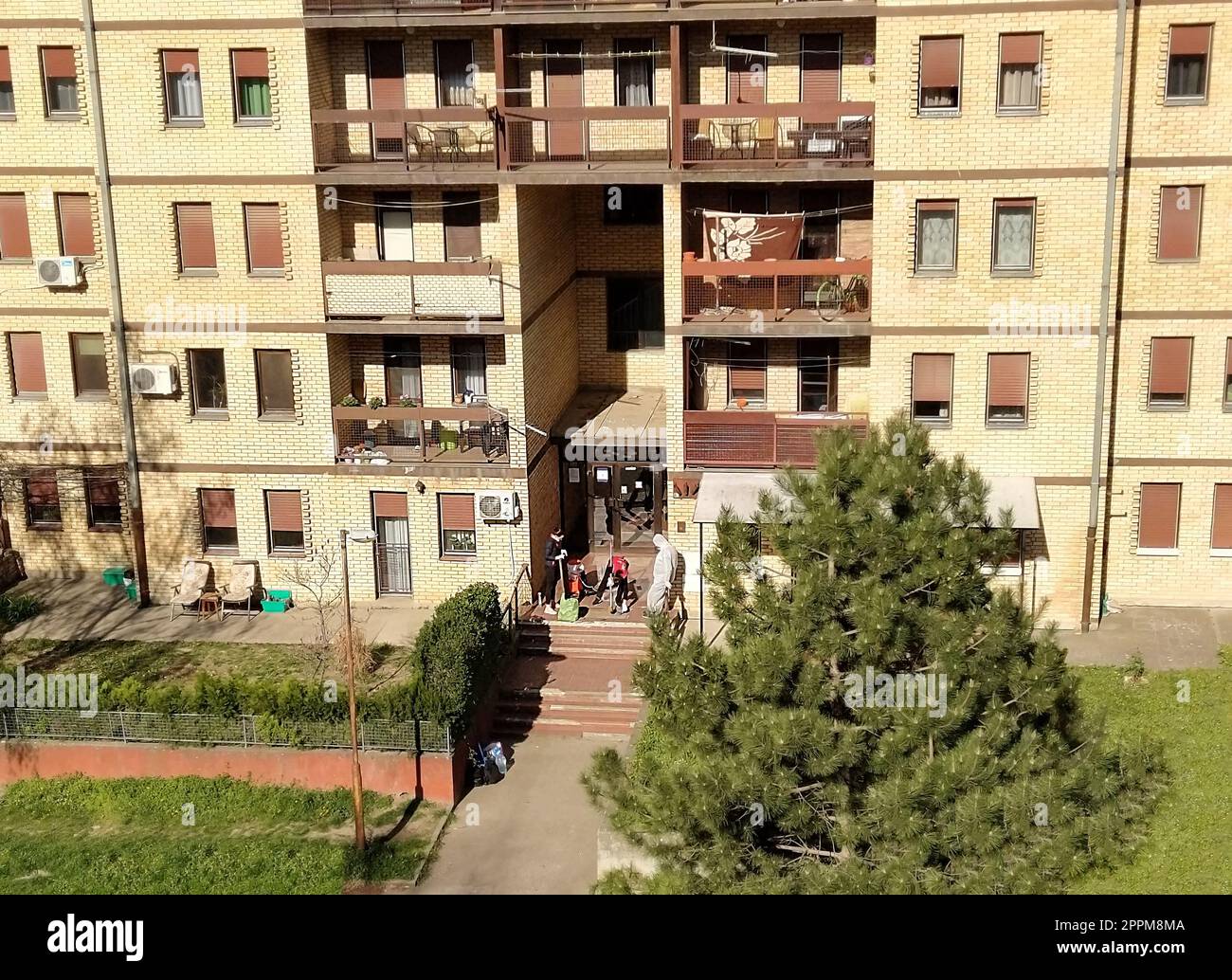 Sremska Mitrovica, Serbien, 08. April 2020 - Desinfektion des Eingangs eines Wohnungsgebäudes durch zwei Frauen - Putzfrauen und eine Epidemiologin in einem weißen biochemischen Schutzanzug. Stockfoto