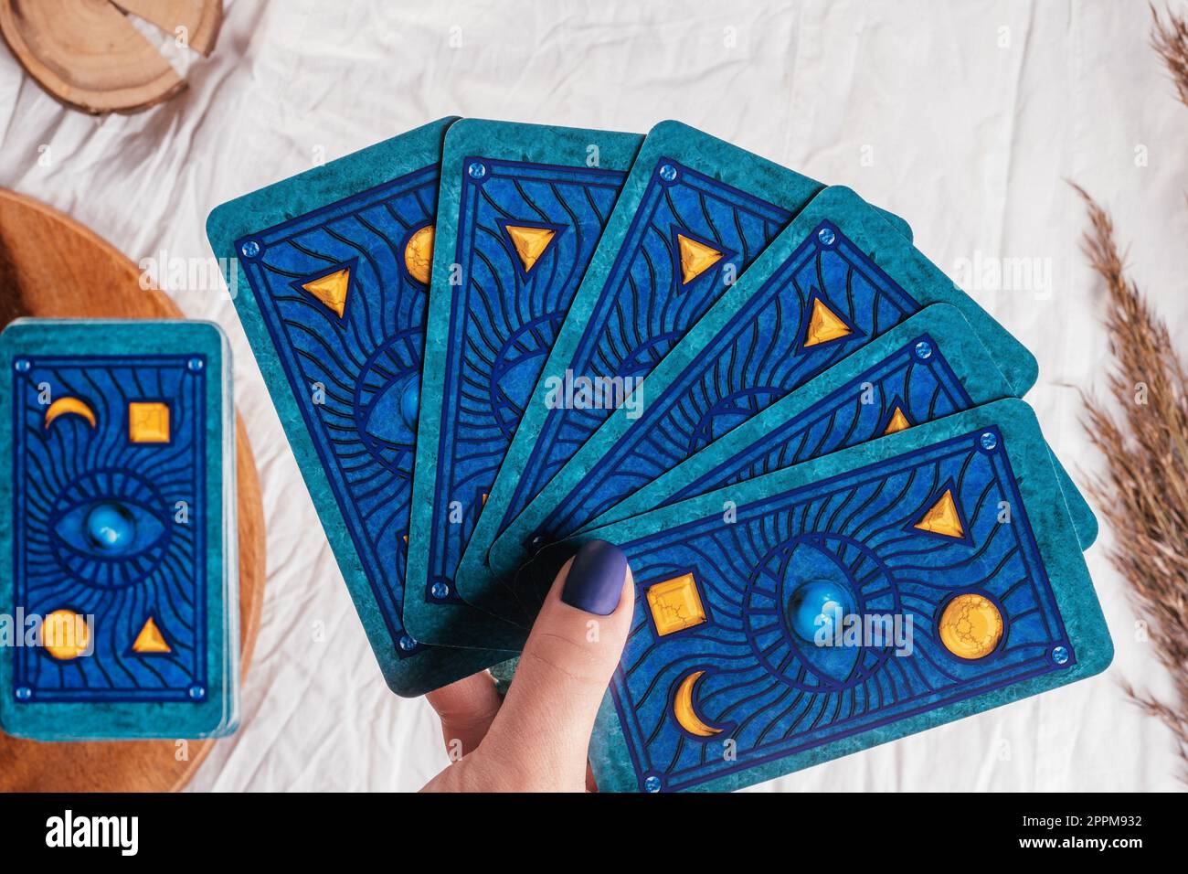 Die Hand mit blauen Nägeln hält Tarotkarten, die über weißes Stofftuch mit Stacheln gefächert sind. Minsk, Belarus - 09.27.2021 Stockfoto