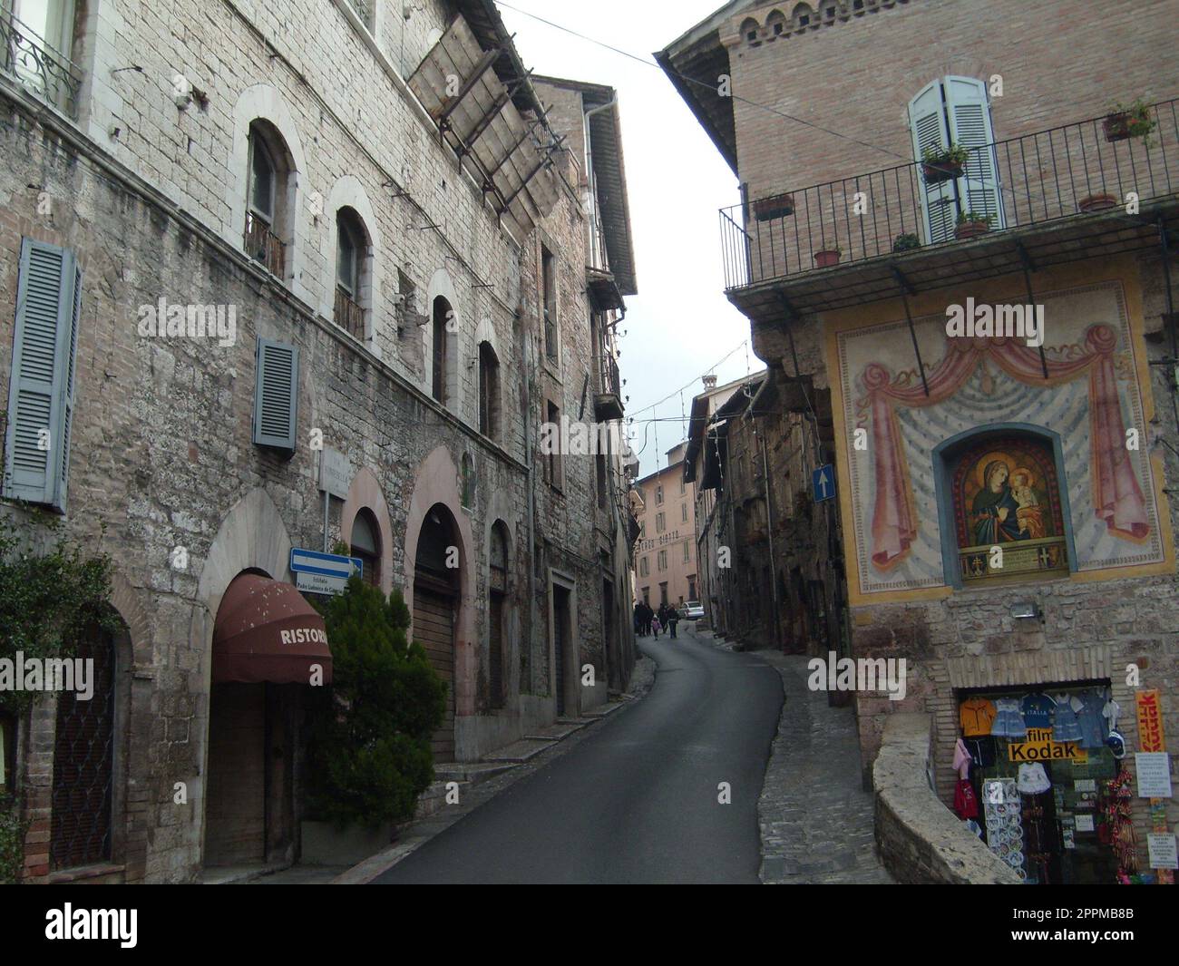 Assisi, Italien, 10. Dezember 2020. Straßen von Assisi, entlang derer eine Gruppe von Touristen zu Fuß geht. Alte Gebäude, nahe beieinander. Leute auf Ausflügen. Enge Straße Stockfoto