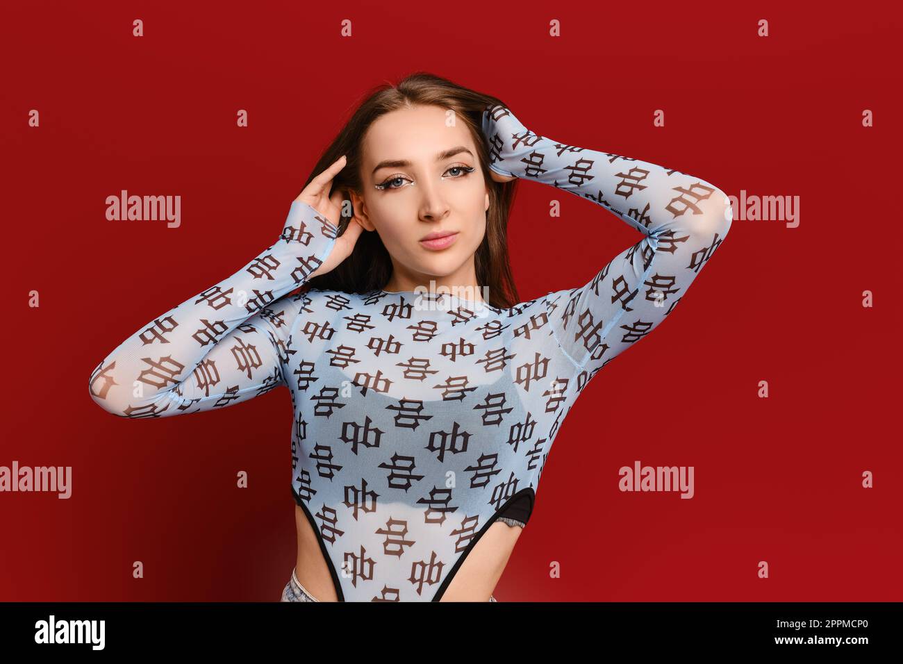 Selbstbewusste junge Frau mit den Händen hinter dem Kopf auf rotem Hintergrund Stockfoto