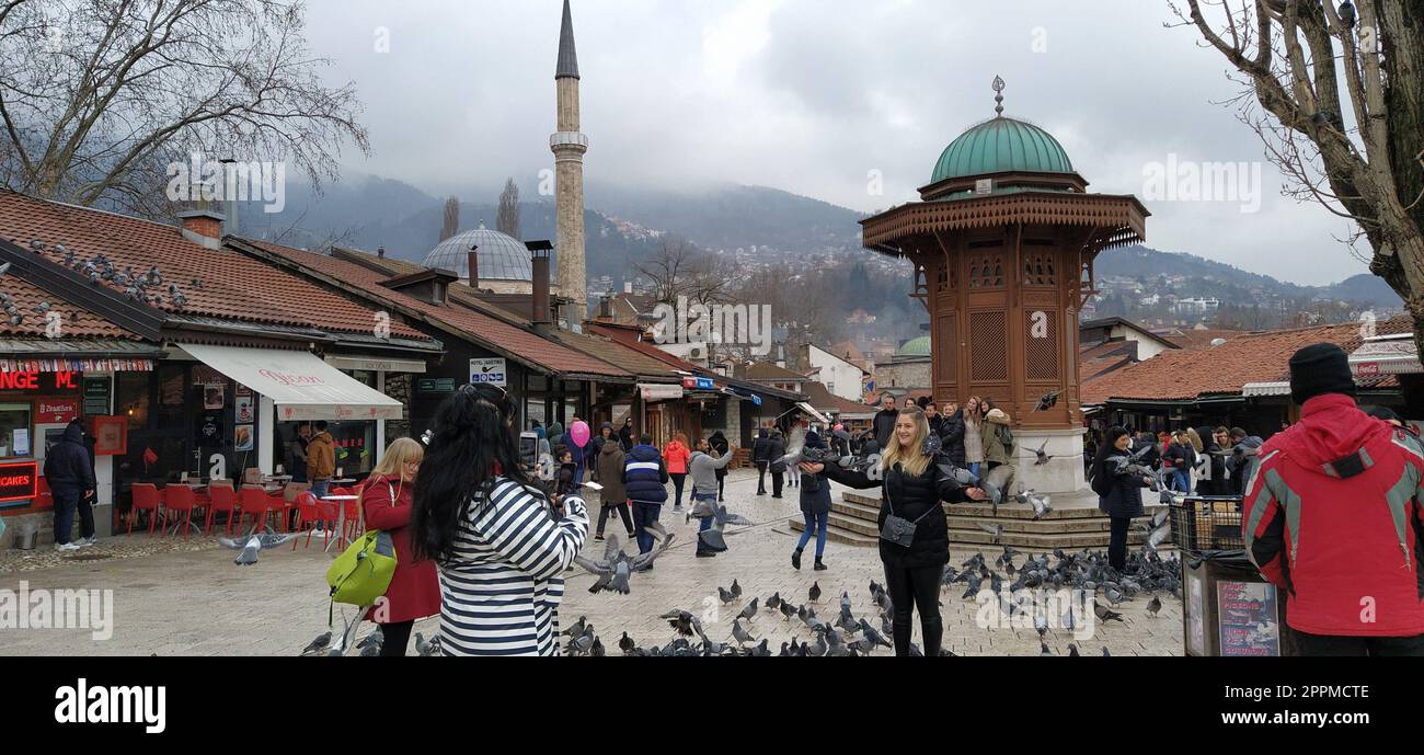 Sarajevo, Bosnien und Herzegowina, 8. März 2020, Menschen gehen durch die zentralen Straßen von Sarajevo und füttern Tauben. Bascarsija und Square. Islamische Wahrzeichen und Touristenattraktionen. Vögel laufen auf dem Bürgersteig Stockfoto