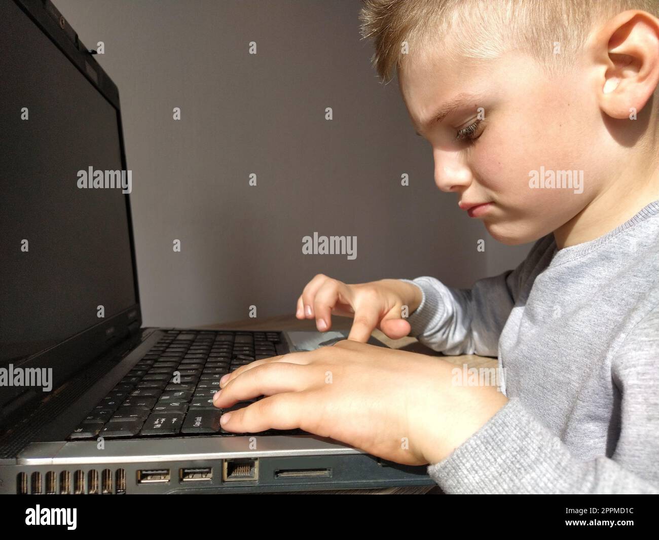 Der kleine Junge mit dem Computer. Der Junge schaltet den Laptop ein. Die schwarze Tastatur. Ein blondes Kind. Nachdenkliches Gesicht. Bildungskonzept. Gadget-Suchtbegriff Stockfoto