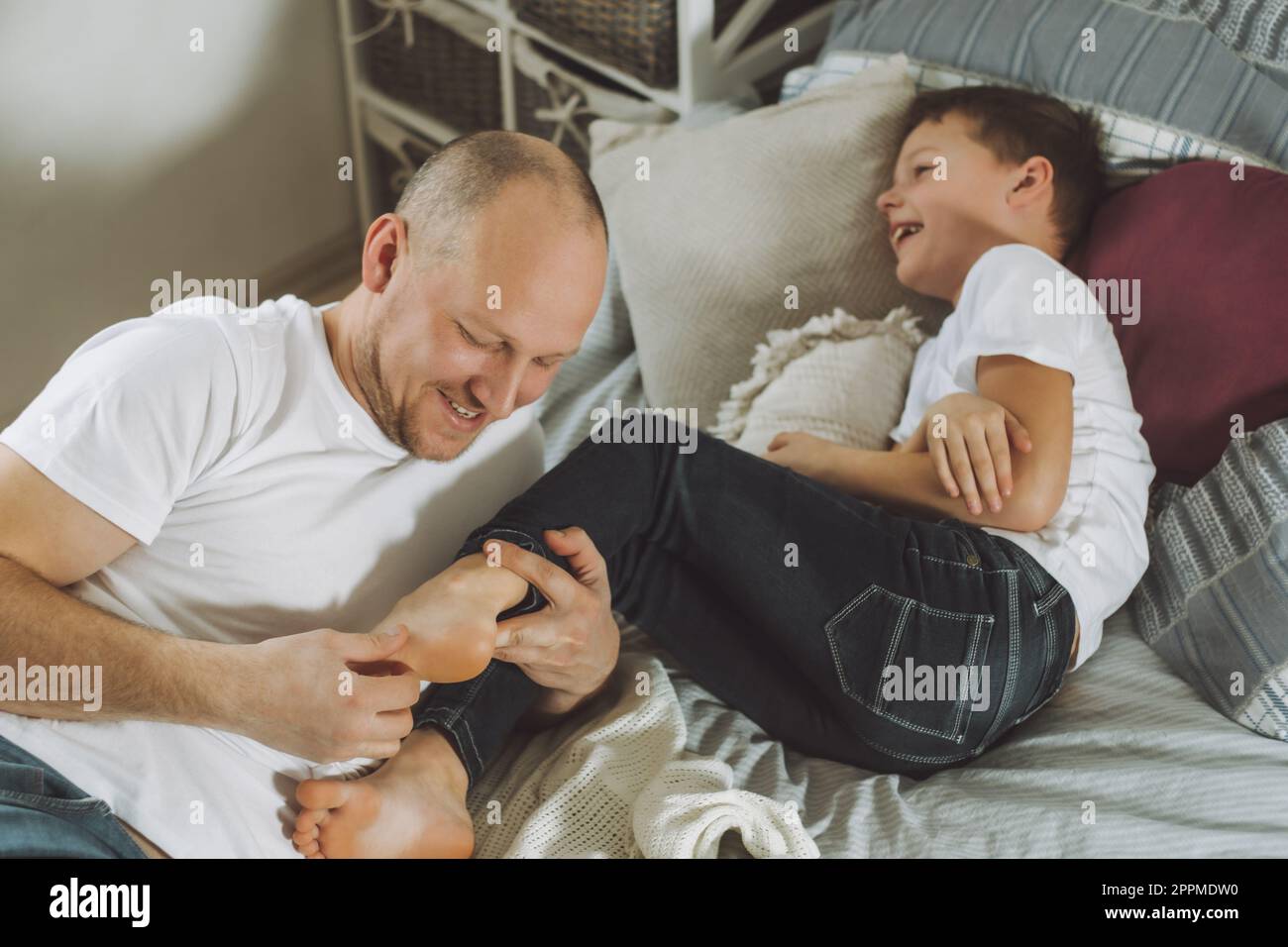 Vater spielt mit seinem Sohn 7-10 im Bett. Dad kitzelt Kinderfüße. Familie, Spaß haben Stockfoto