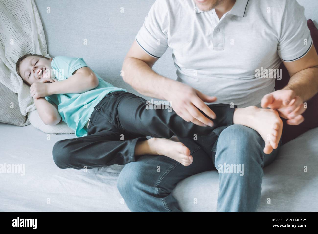 Vater spielt mit seinem Sohn 7-10 auf der Couch. Dad kitzelt Kinderfüße. Familie, Spaß haben Stockfoto