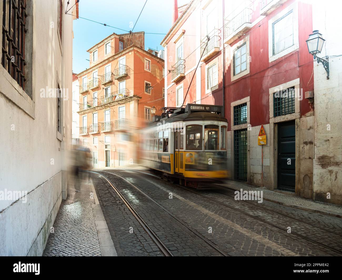 Gelbe Straßenbahn in Lissabon, die bei Sonnenaufgang schnell in einer kleinen Straße im Zentrum der Stadt fährt Stockfoto