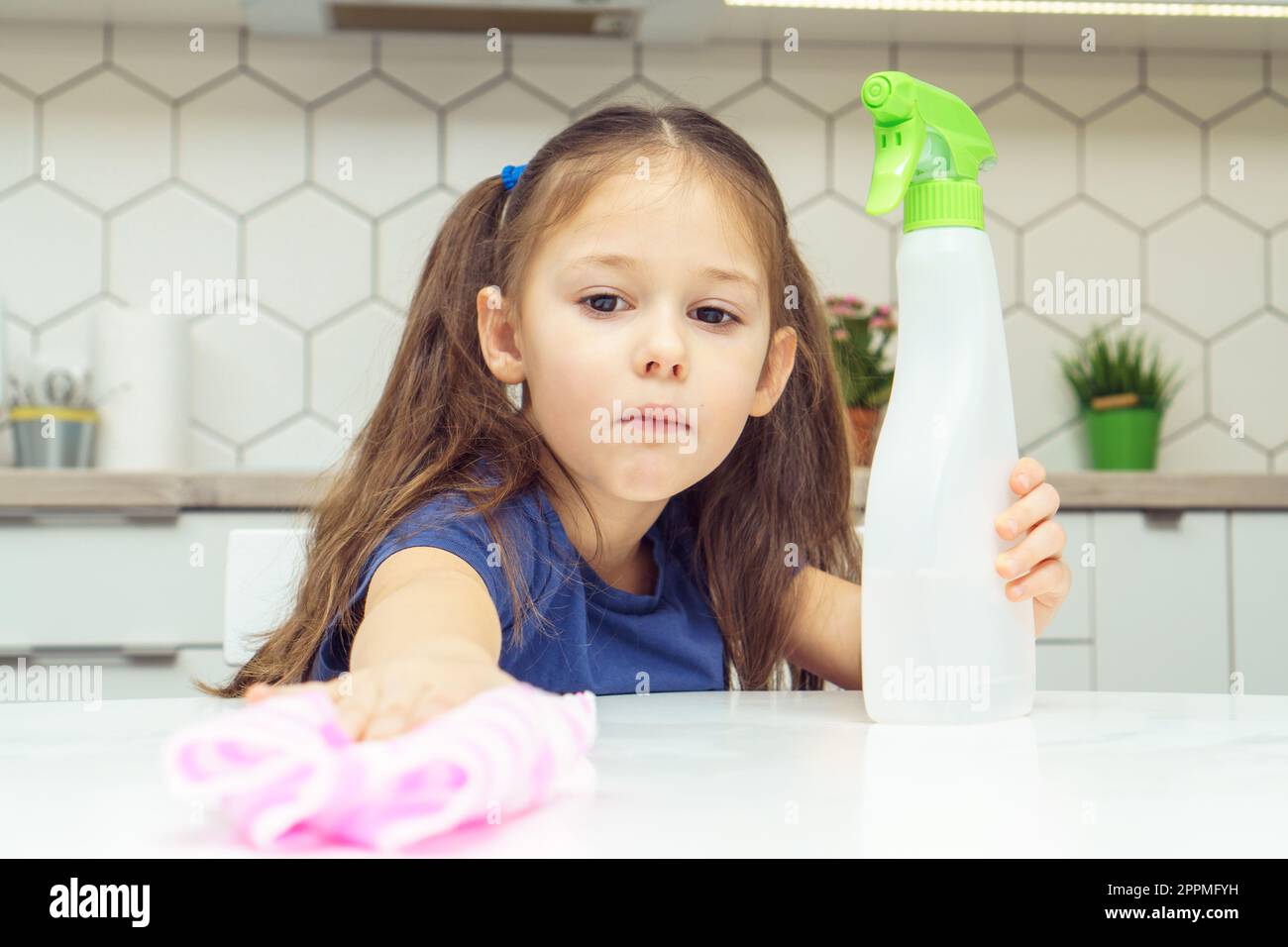 Hübsches kleines Mädchen mit Waschmittel-Sprühgerät und Haushaltslappen-Wischtisch. Kind räumt Küche auf, Haushalt putzen. Stockfoto