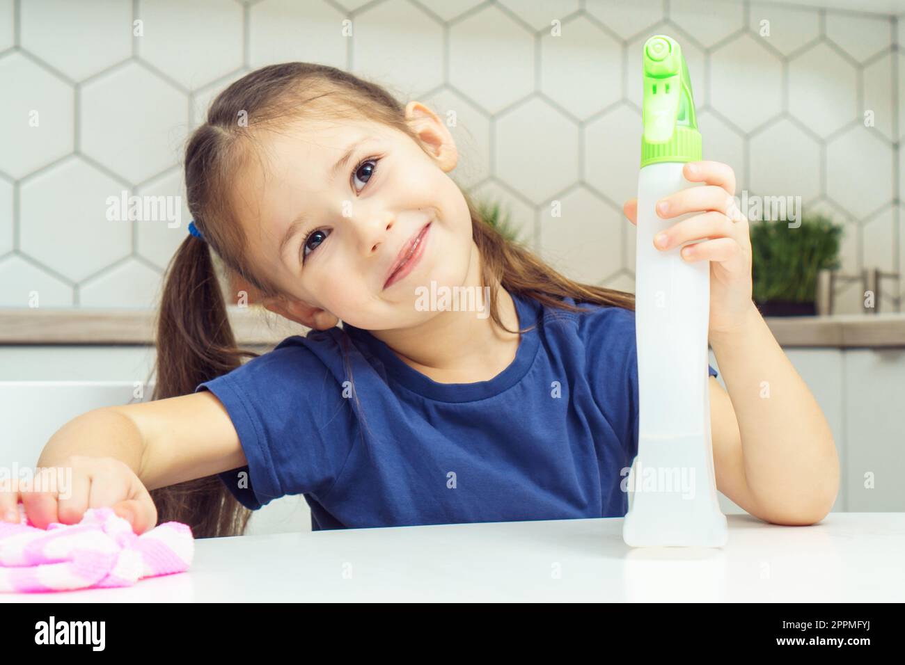 Glückliches kleines Mädchen mit Reinigungsspray und Haushaltstücher am Tisch. Porträt eines Kindes, das Küche aufräumt, Hausreinigung Stockfoto