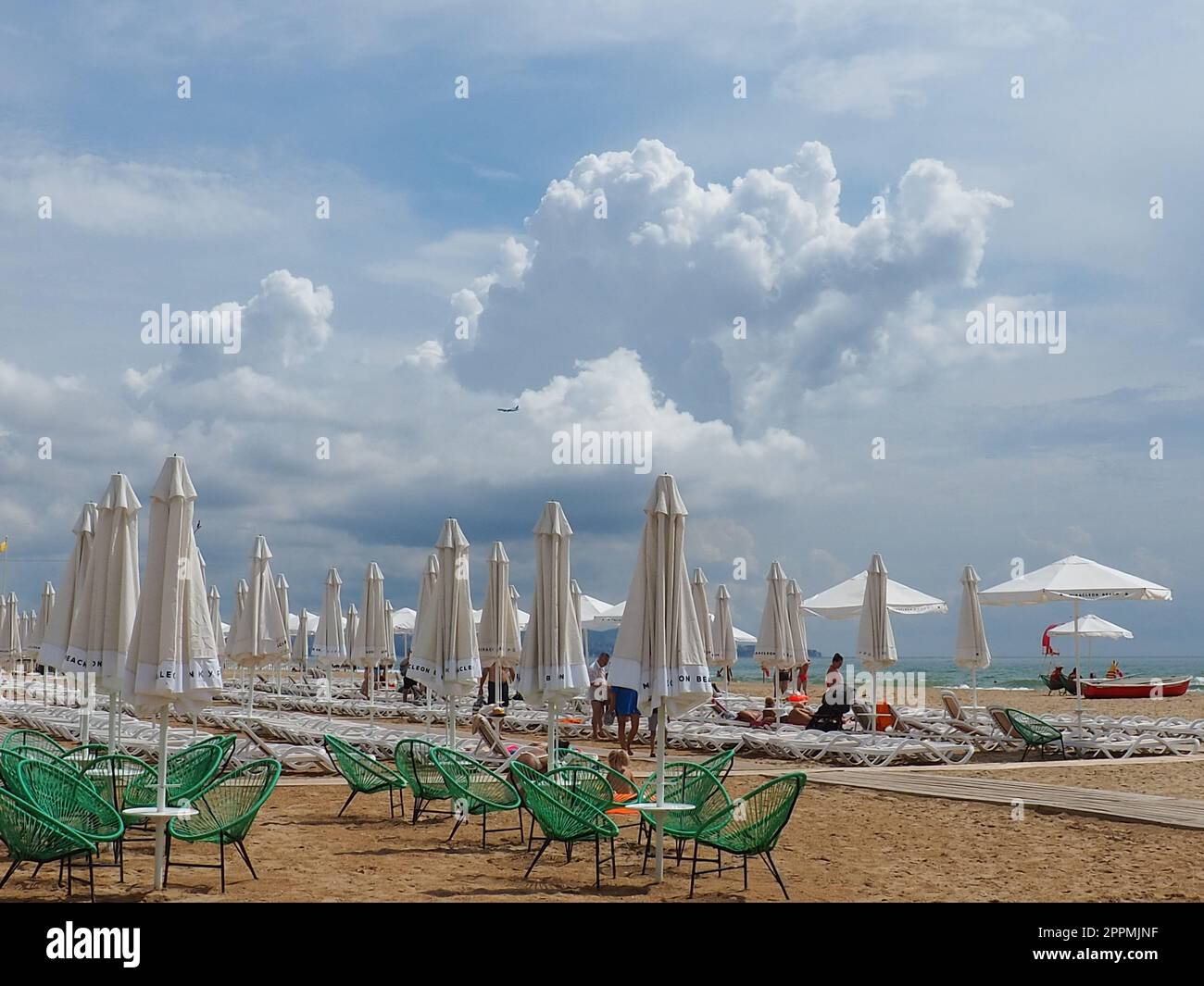 Anapa, Russland, 15. August 2021 Sonnenliegen und Sonnenschirme am Sandstrand nach dem Regen. Strandsaison. Strandcafe mit Korbstühlen. Touristen, die Leute laufen lassen. Eine Sturmwarnung. Kumuluswolken Stockfoto
