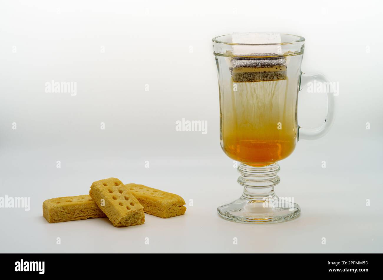 Heißer Tee, der in einem klaren Becher mit Strähnen aus Teeessenz serviert wird und das Wasser mit dem wunderbaren Geschmack der Blätter und Short-Brote erfüllt Stockfoto