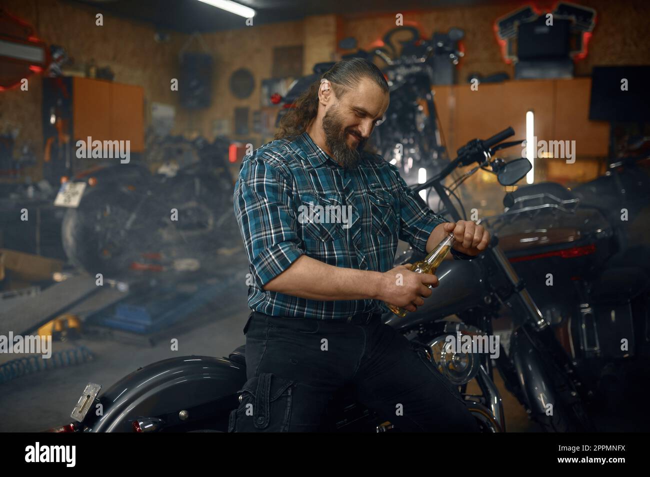 Reifer Biker trinkt Bier in seiner Werkstatt Stockfoto