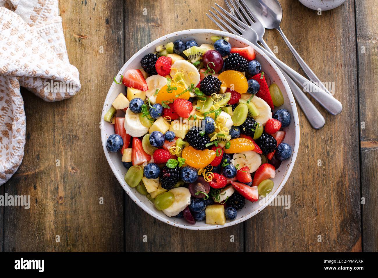 Obstsalat auf einem Holztisch mit Beeren, Zitrusschale, Minze und Honigdressing, Blick über den Kopf Stockfoto
