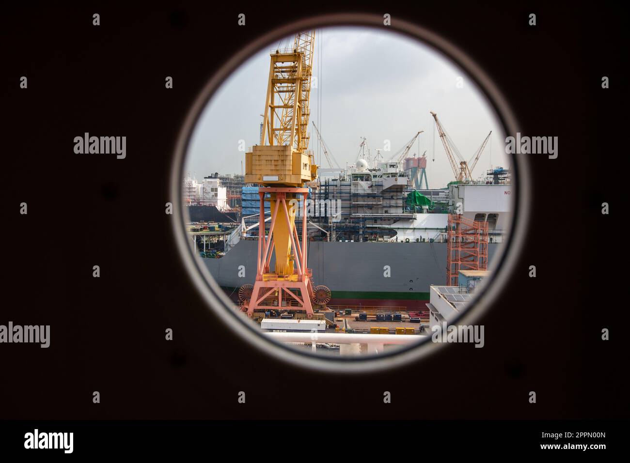 Durch das runde Fenster blickt der gigantische Kran der Werft in Betrieb für den Bau, die Herstellung oder die Reparatur eines Schiffes. Singapur. Stockfoto