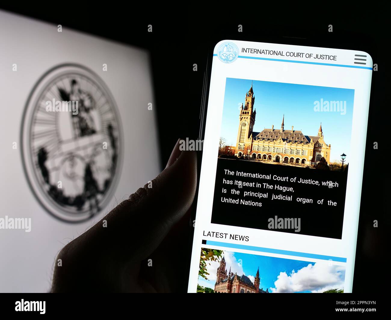 Person, die ein Mobiltelefon mit einer Website des Internationalen Gerichtshofs (IStGH) auf dem Bildschirm vor dem Logo hält. Konzentrieren Sie sich auf die Mitte des Telefondisplays. Stockfoto