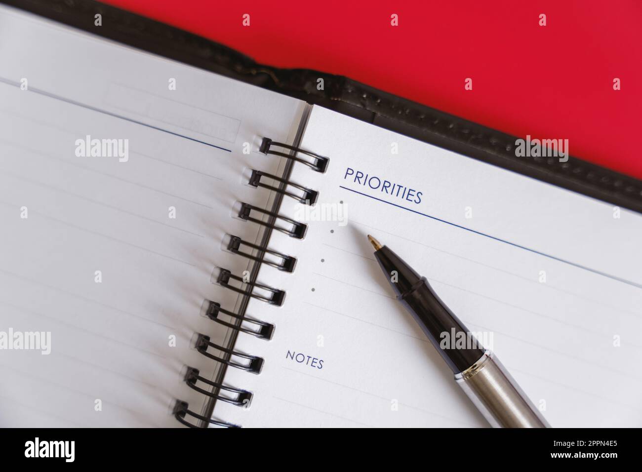 „Daily Planning with Personal Planner“ (tägliche Planung mit persönlichem Planer) – ein persönlicher Planer und Stift für die tägliche Planung auf rotem Hintergrund. Stockfoto