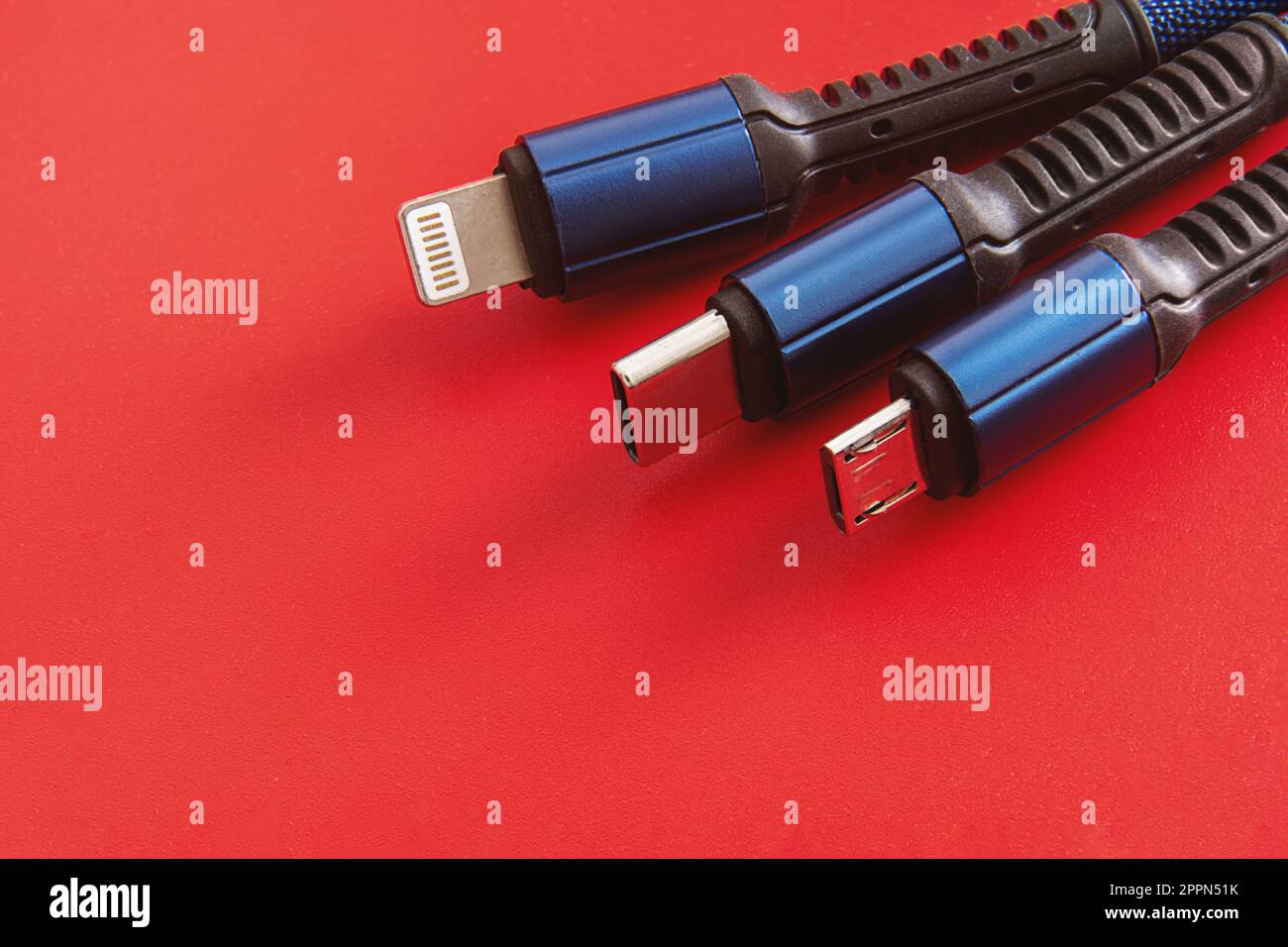 „USB-Kabel auf rotem Hintergrund“ – Nahaufnahme von USB-C-, Lightning- und Micro-USB-Kabeln mit schwarzen und blauen Farben auf rotem Hintergrund. Stockfoto