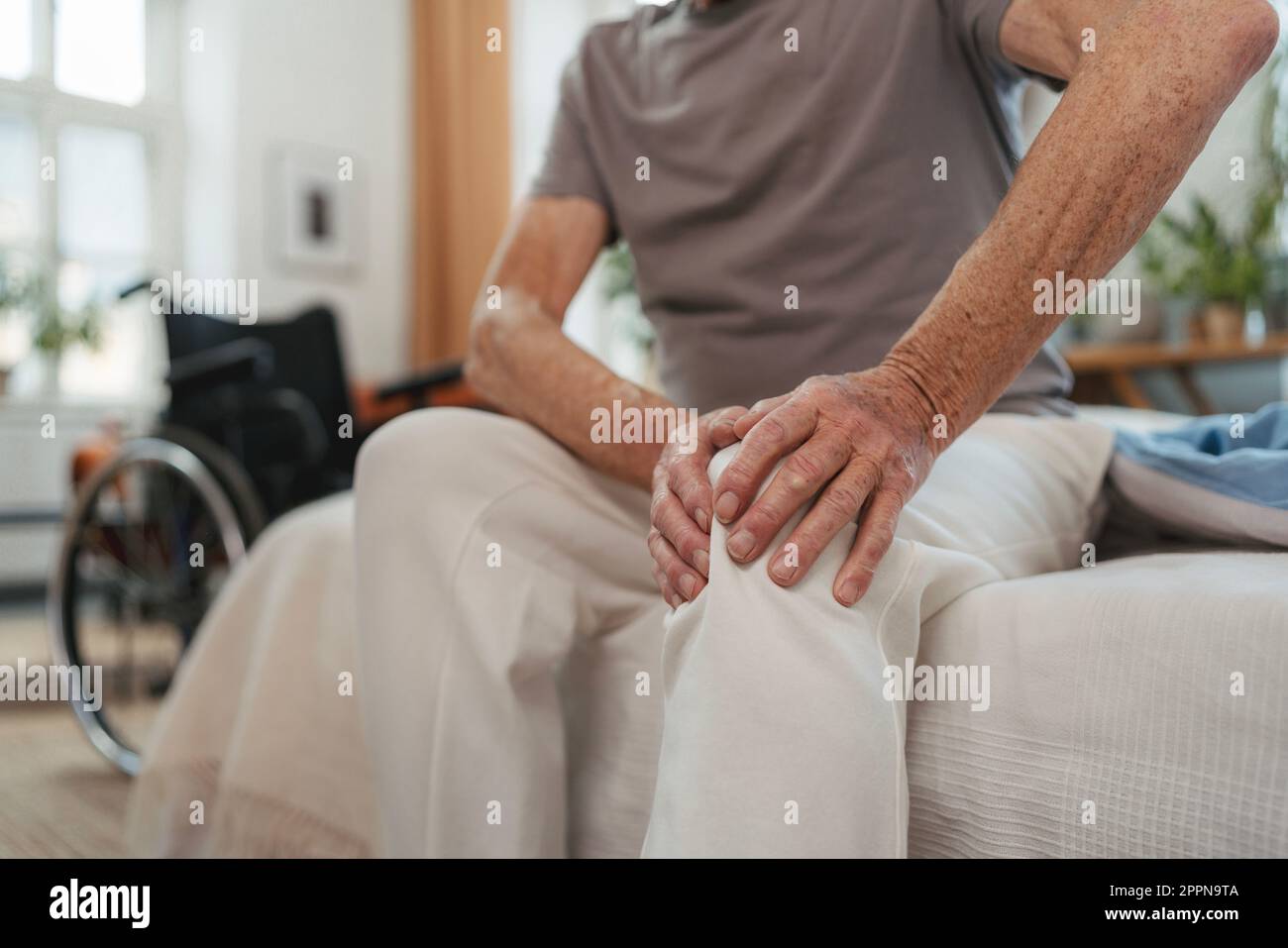 Nahaufnahme eines Seniorenmannes mit Knieschmerzen, der auf einem Bett sitzt. Stockfoto
