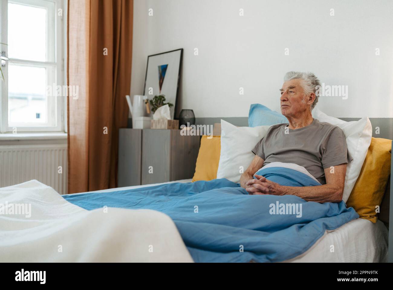 Seniorenmann, der allein im Bett sitzt, Begriff der Einsamkeit und der psychischen Gesundheit. Stockfoto