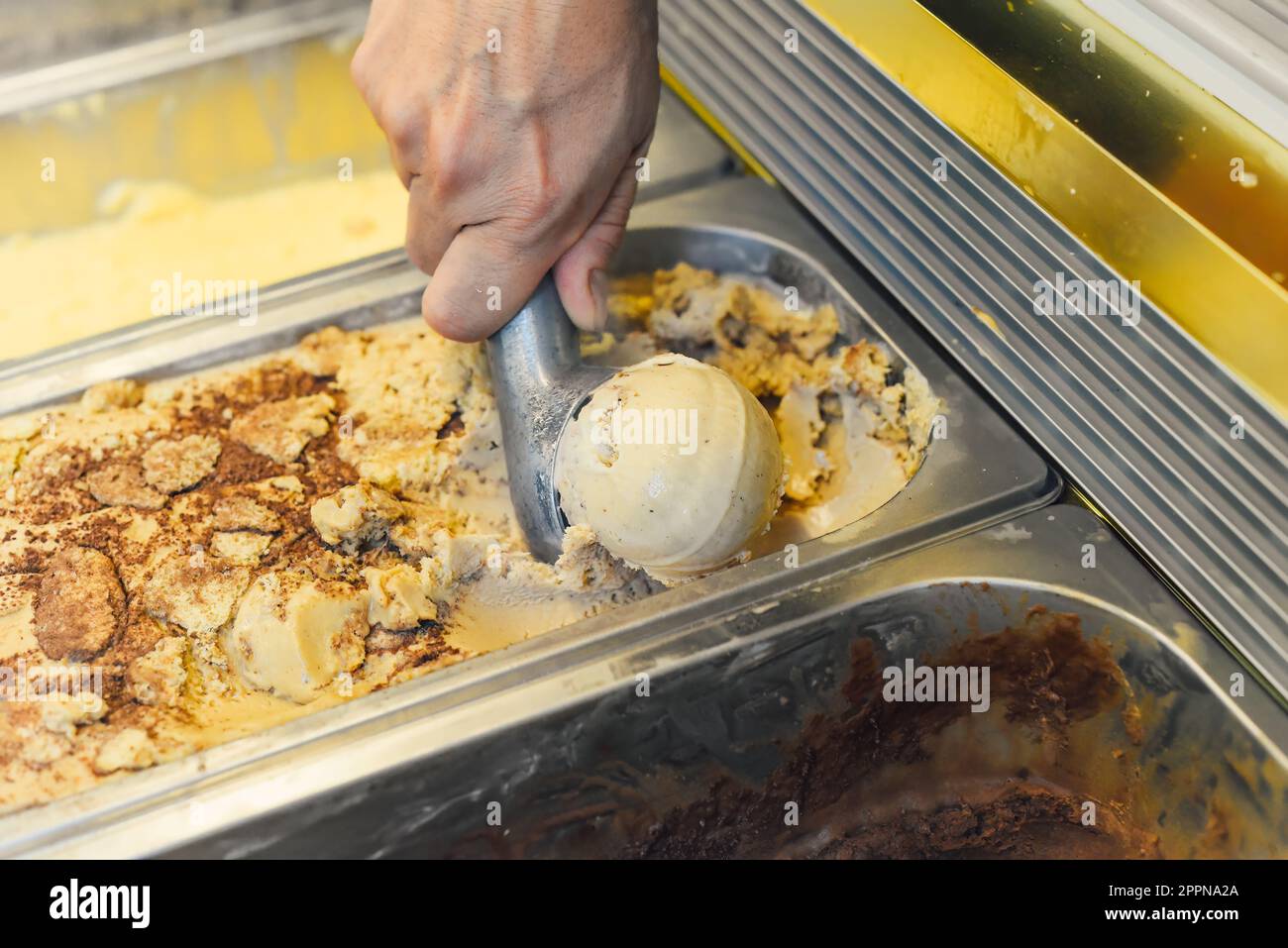 Mit der Hand eine Kugel Eiscreme in einen Löffel im Kühlschrank schöpfen Stockfoto