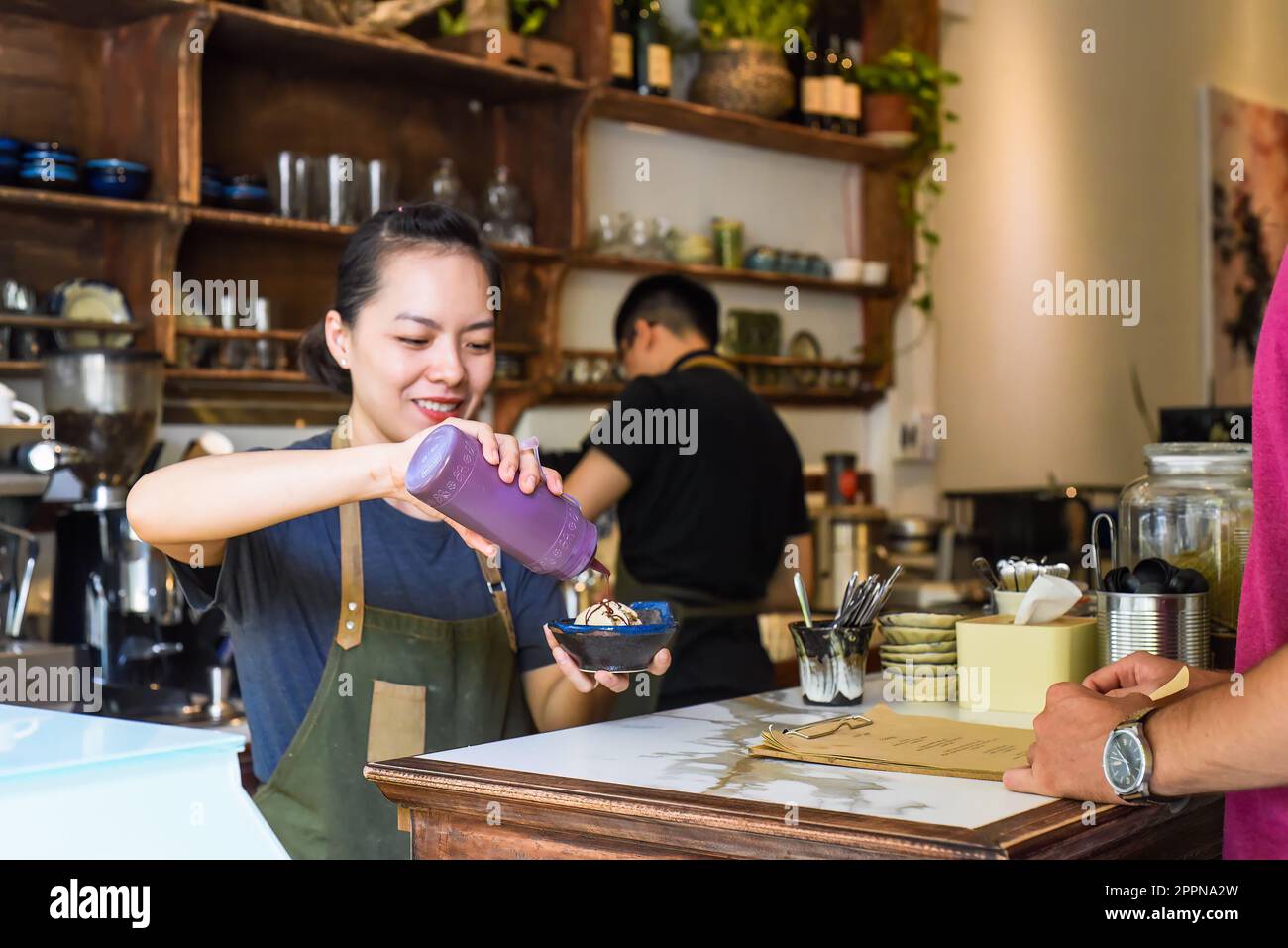 Vietnamesische Kellnerin, die einem Kunden in einem Café Eiscreme serviert Stockfoto