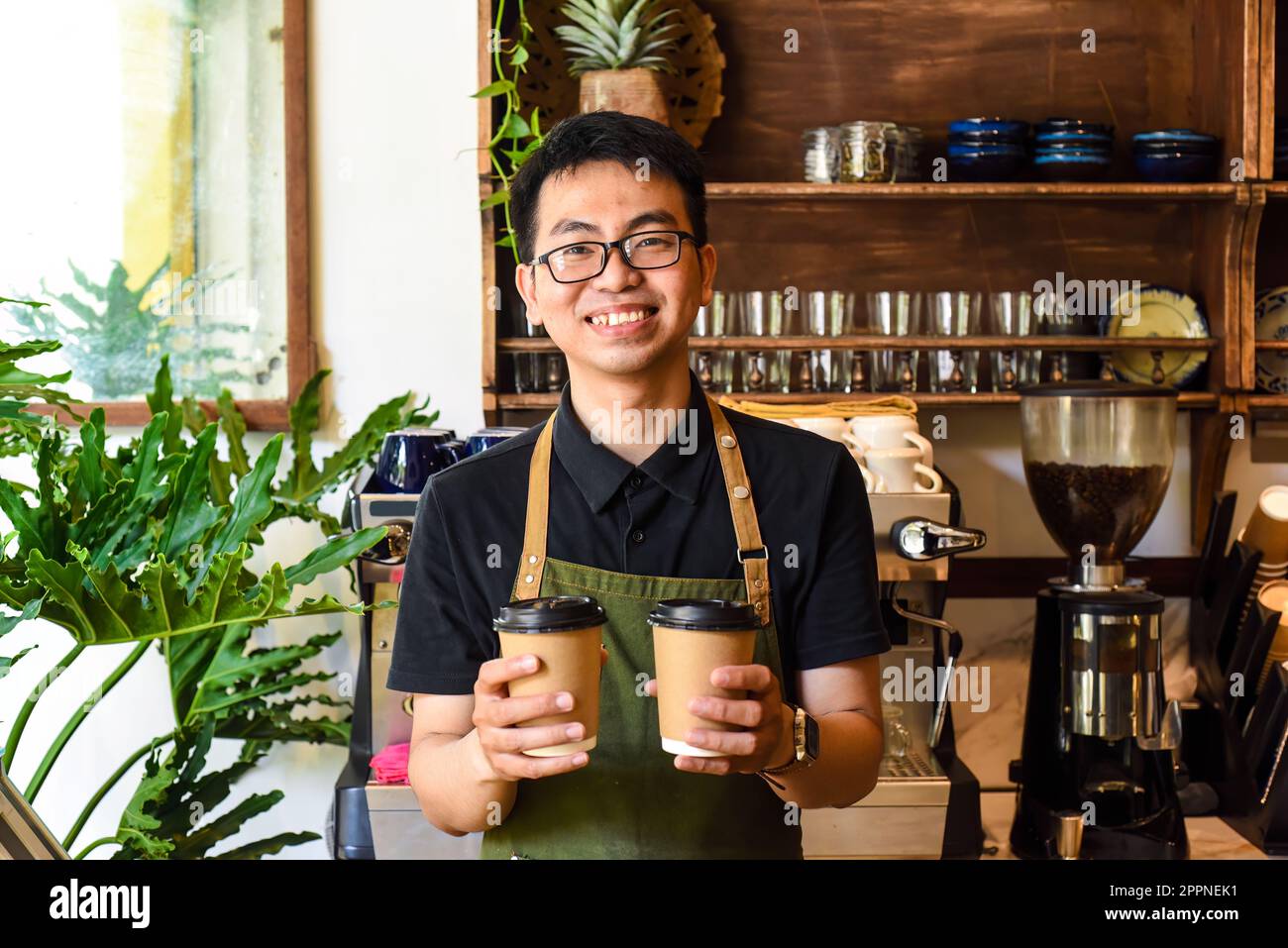 Vietnamesischer lächelnder Kellner hielt Pappbecher mit Kaffee in einem Café Stockfoto
