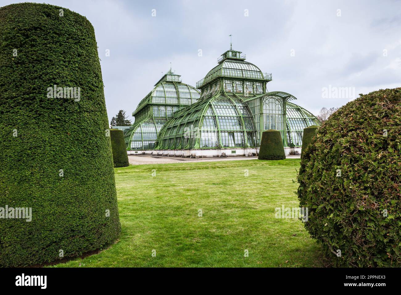 Die Kuppeln des Palmenhauses aus Schmiedeeisen, Gusseisen und Glas im Schlosspark Schönbrunn unter grauem Himmel, Wien, Österreich Stockfoto