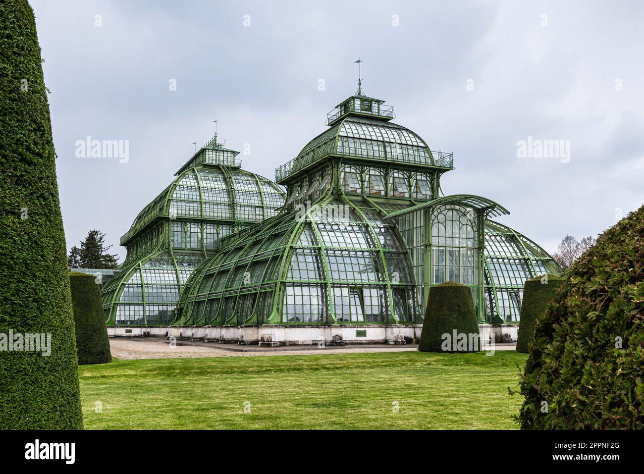 Die Kuppeln des Palmenhauses aus Schmiedeeisen, Gusseisen und Glas im Schlosspark Schönbrunn unter grauem Himmel, Wien, Österreich Stockfoto