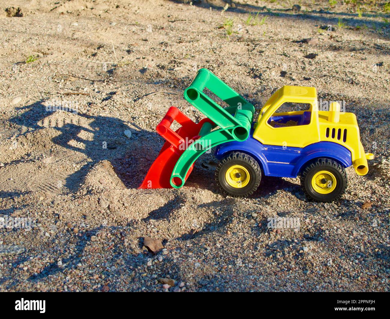 Plastik-Spielzeugwagen mit Schatten im Sandkasten auf dem Kinderspielplatz im Sommer im Freien. Stockfoto