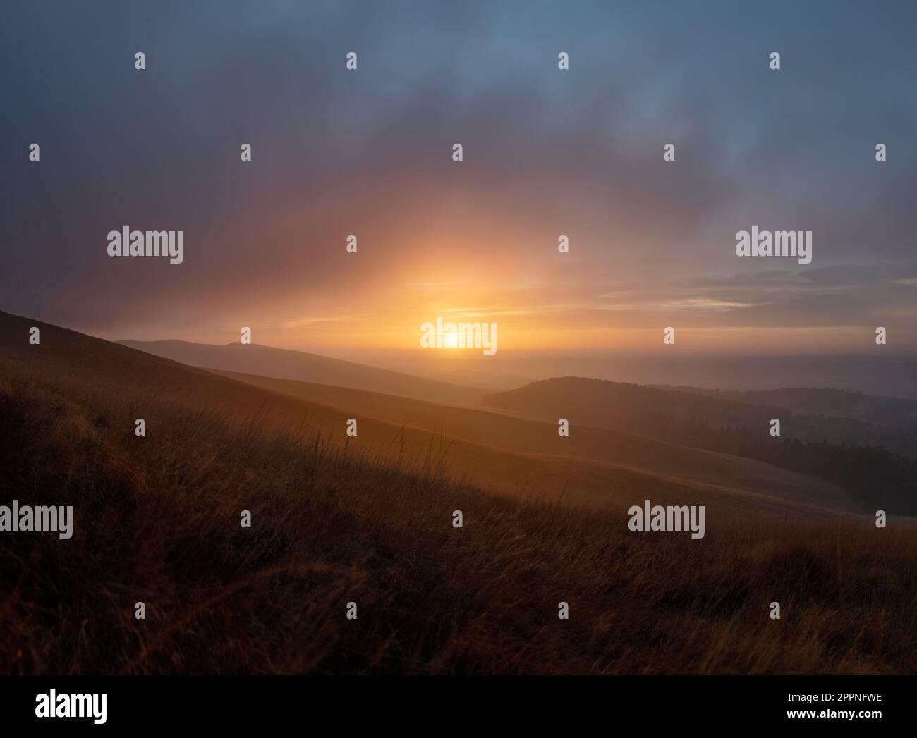 Sonnenuntergang über grasbedeckten Moorlandschaften im Peak District mit Blick auf die Cheshire Plains. Der Sonnenuntergang erhellt die Wolken mit warmen Farben Stockfoto