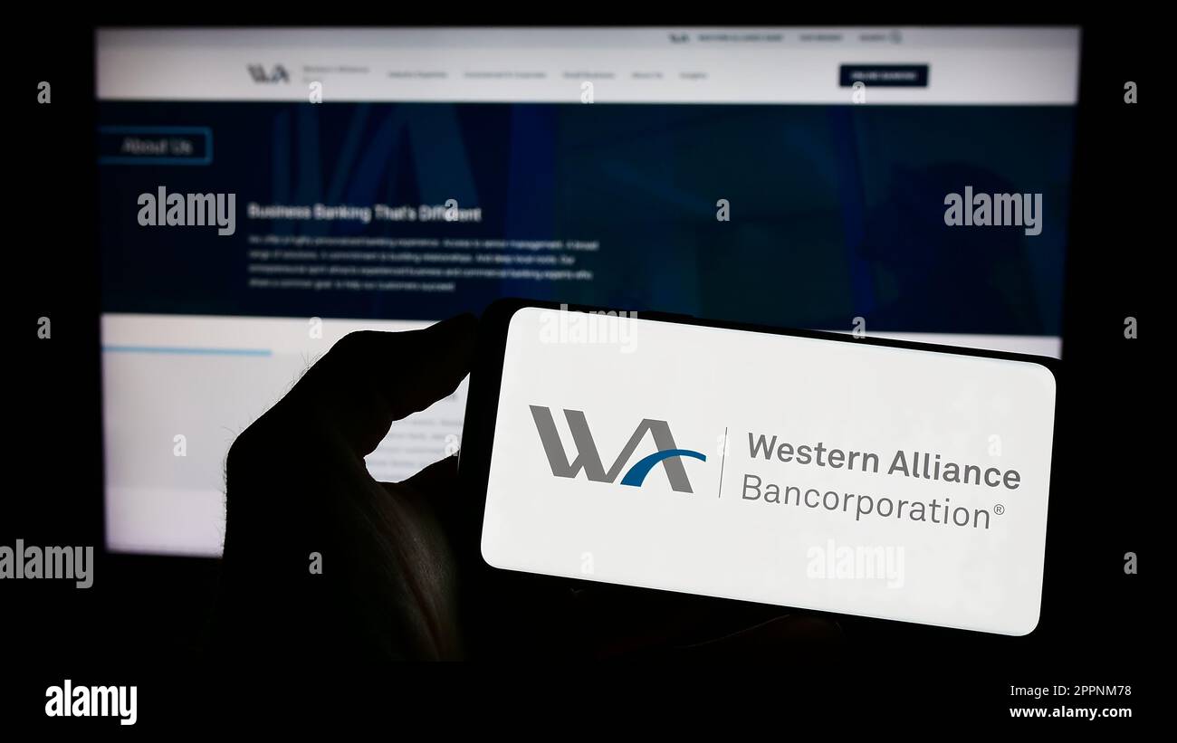 Person, die ein Mobiltelefon mit dem Logo der amerikanischen Firma Western Alliance Bancorporation auf dem Bildschirm vor der Webseite hält. Konzentrieren Sie sich auf das Display des Telefons. Stockfoto