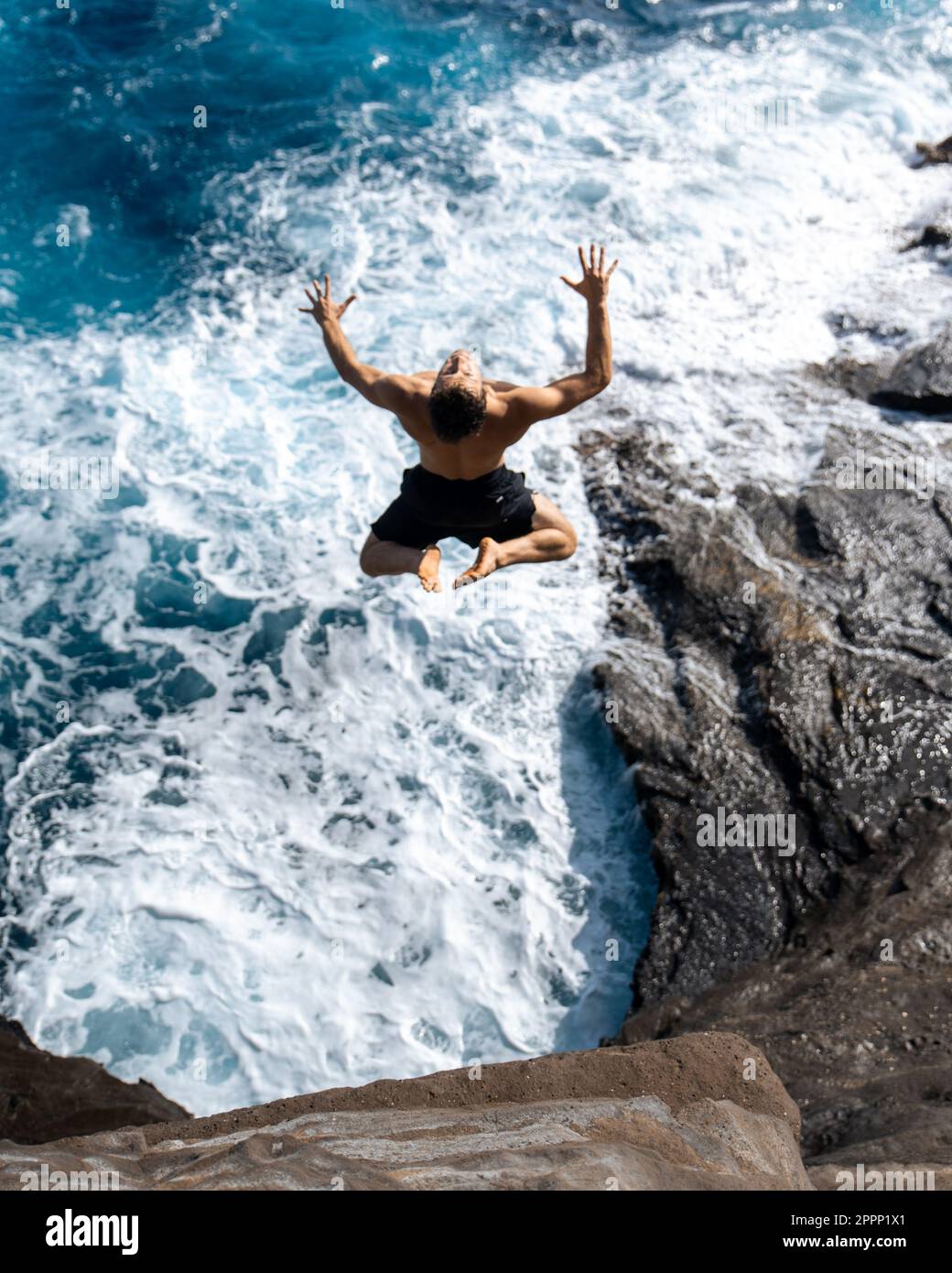 Ein Mann, der von der Spitting Cave auf Oahu, Hawaii, springt. Hochwertiges Foto Stockfoto
