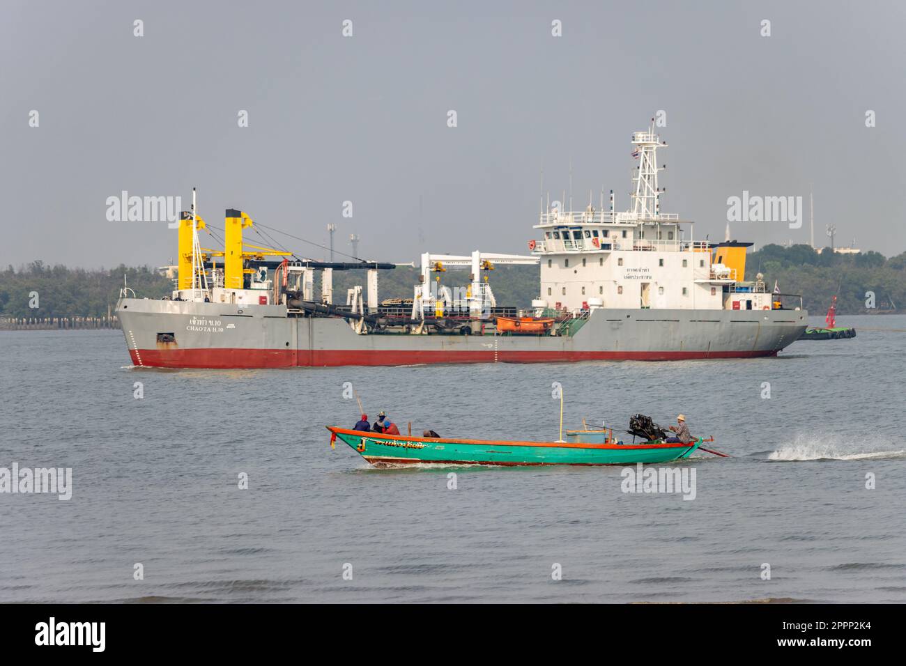 SAMUT PRAKAN, THAILAND, MÄRZ 14 2023, Ein Fischerboot segelt auf dem Chao Phraya River, ein Baggerboot im Hintergrund Stockfoto