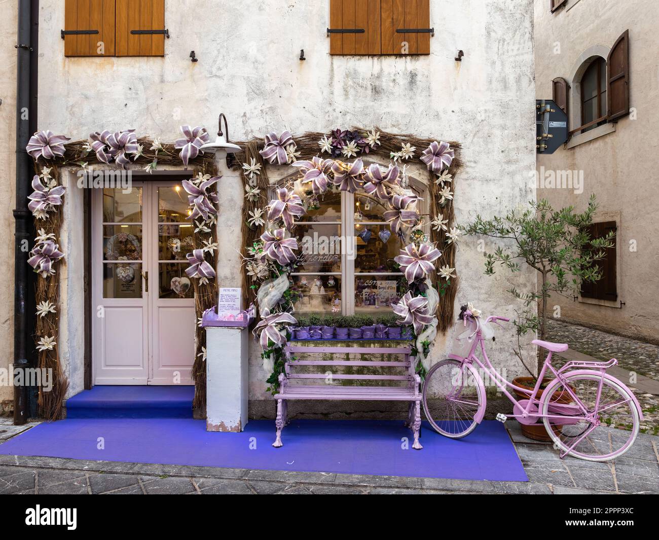 Venzone, Italien - 29. Dezember 2022: Lavendelgeschäft in der mittelalterlichen Stadt Venzone, Friuli und ein dekoratives rosa Fahrrad Stockfoto