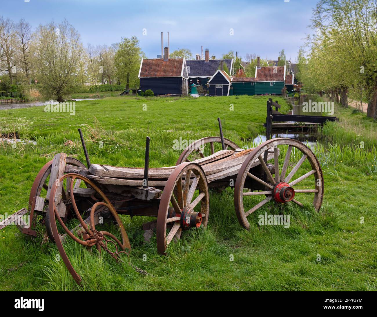 Eine wunderschöne ländliche Landschaft in Hollands Zaanse Schans, mit einem Holzwagen und einem Gebäude umgeben von Feldern mit grünem Gras und Pflanzen. Stockfoto