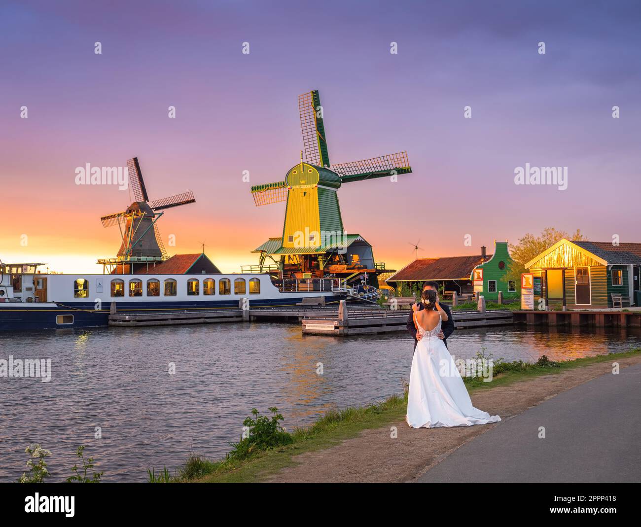 Zaanse Schans, Niederlande - 25. April 2022: Bräutigam und Braut bei Sonnenuntergang inmitten idyllischer niederländischer Windmühlen Stockfoto