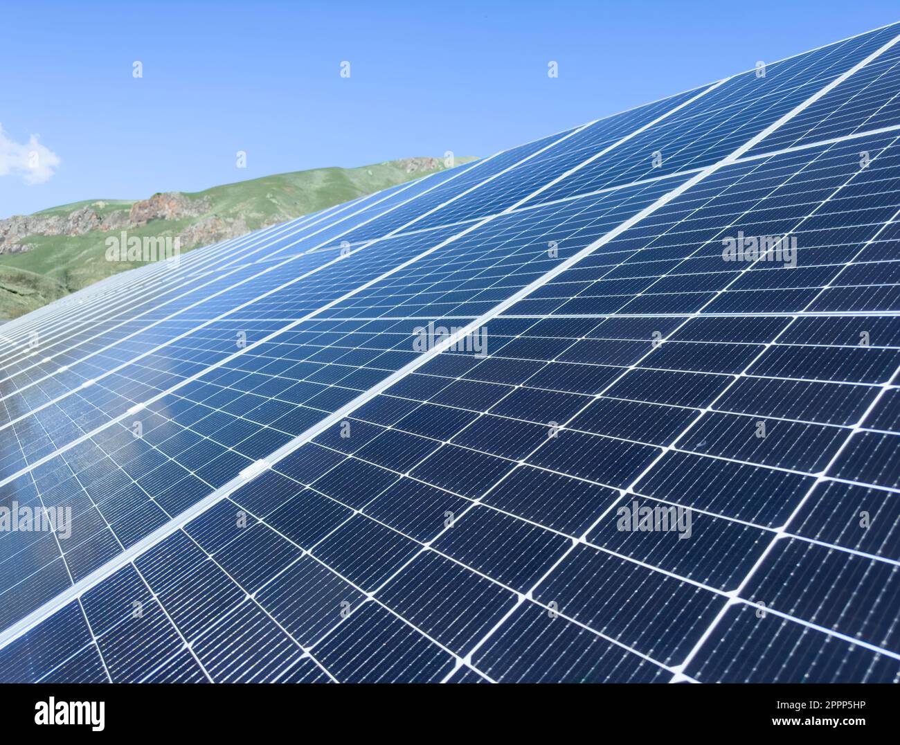 Blaue Sonnenkollektoren über blauem Himmel, Bergen, Sonne und Wolken. Solarpaneele für nachhaltige Energie. Erneuerbare Solarenergie. Alternative Energie. Stockfoto