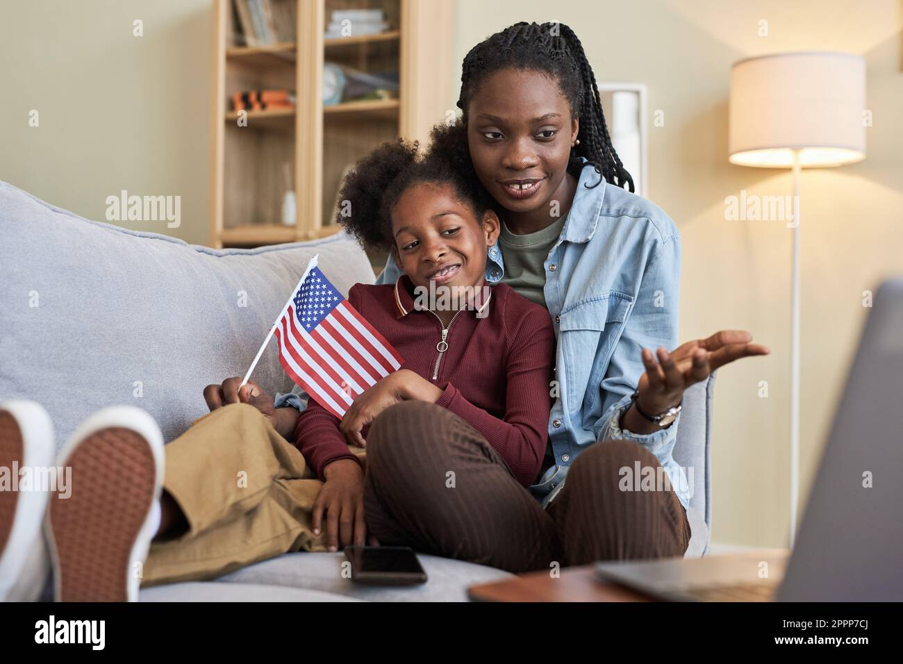 afroamerikanische mutter und Tochter unterhalten sich online auf einem Laptop, während sie auf dem Sofa im Wohnzimmer sitzen Stockfoto