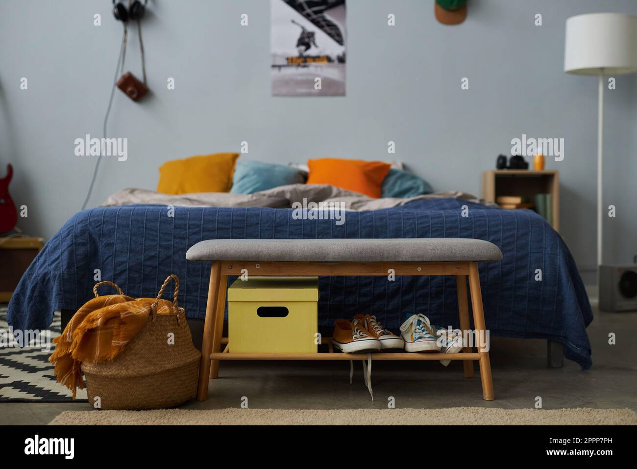 Weiche graue Bank mit zwei Paar neuen Gummischuhen und gelbem Kasten vor einem komfortablen Doppelbett mit einer Gruppe Kissen im Schlafzimmer Stockfoto