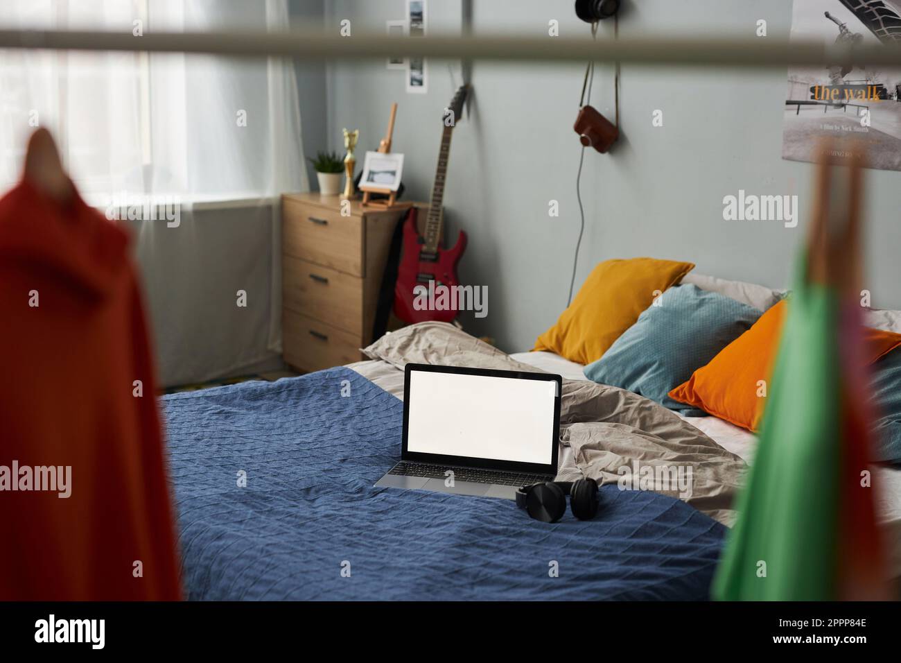 Laptop mit leerem Bildschirm auf einem Doppelbett mit mehreren Kissen und blauer Decke im geräumigen Schlafzimmer des modernen Apartments Stockfoto