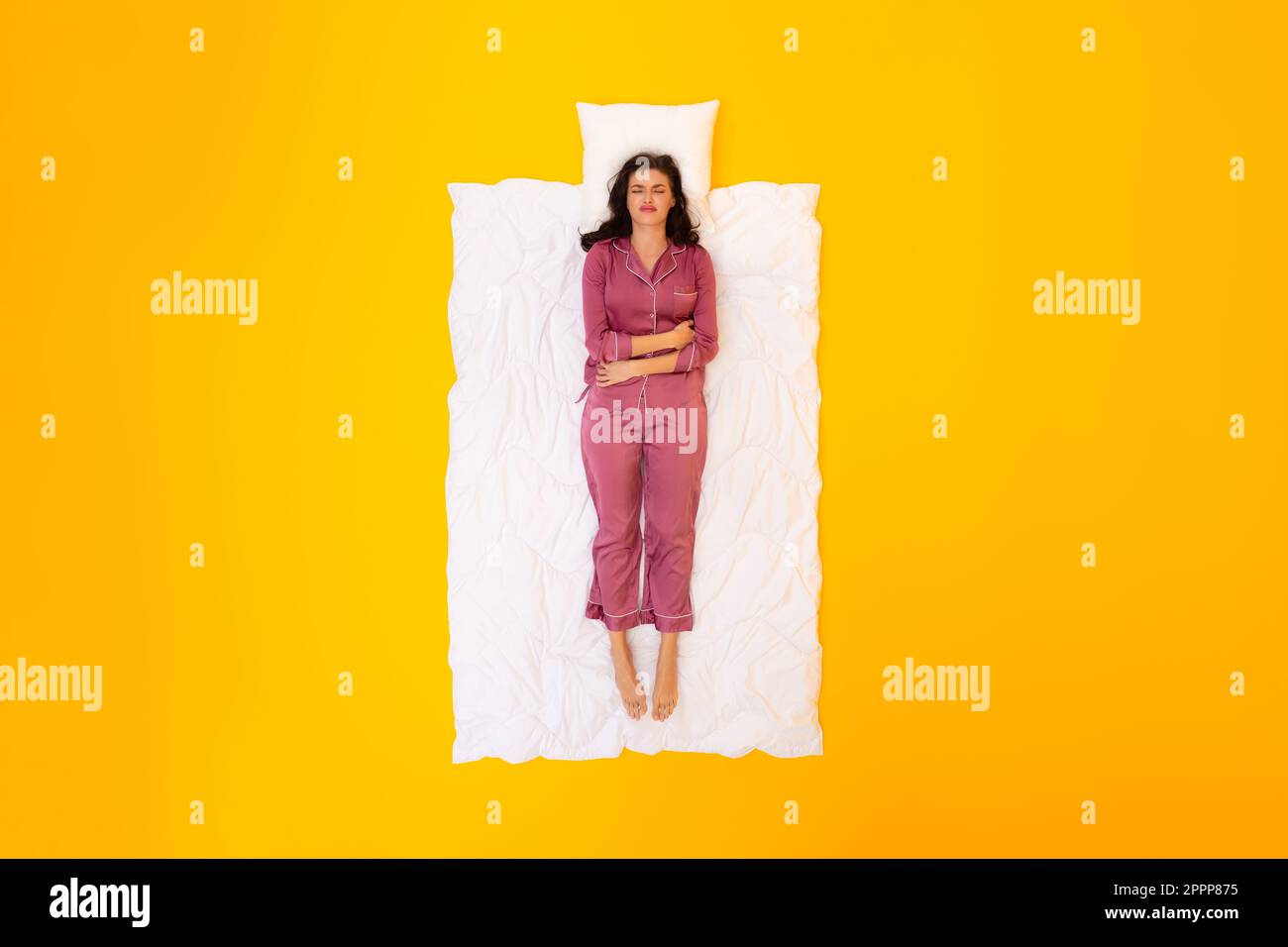 Die Dame kann nicht schlafen und leidet an Menstruationskrämpfen, die lügen, gelber Hintergrund Stockfoto