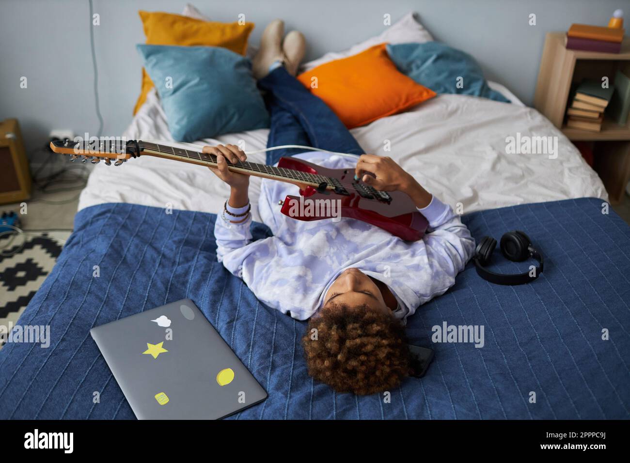 Entspannter afroamerikanischer Teenager, der nach der Schule auf einem bequemen Doppelbett spielt und seine Freizeit genießt Stockfoto