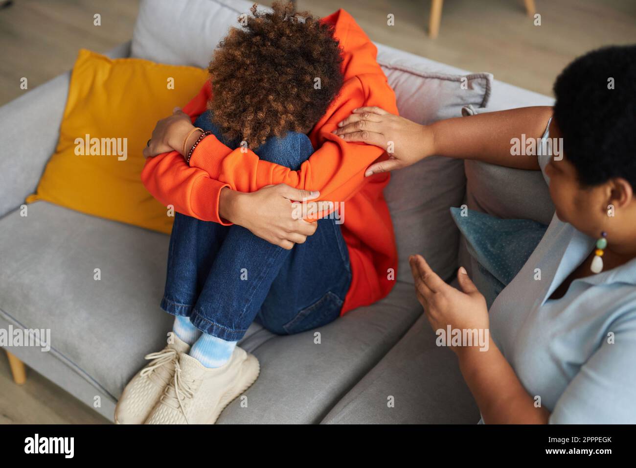 Reife Frau, die auf der Couch neben einem depressiven Teenager-Kerl in Freizeitkleidung sitzt und seine Schulter berührt, während sie ihn tröstet Stockfoto